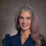 Elaine is smiling and has long hair and wearing a blue shirt.