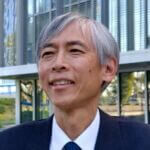 Glenn has short gray hair and is smilling and wearing a dark suit and tie