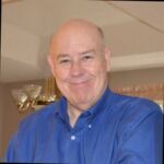 Headshot of Jack grinning and wearing a blue shirt