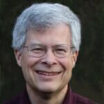 Jim has short gray hair and glasses and is smiling