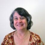 Marsha has medium length hair and is smiling and wearing a floral top