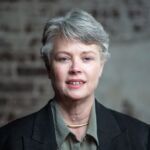 Robin is smiling and has short hair and is wearing a black jacket