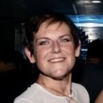 Sandra has short dark hair and is wearing a white shirt